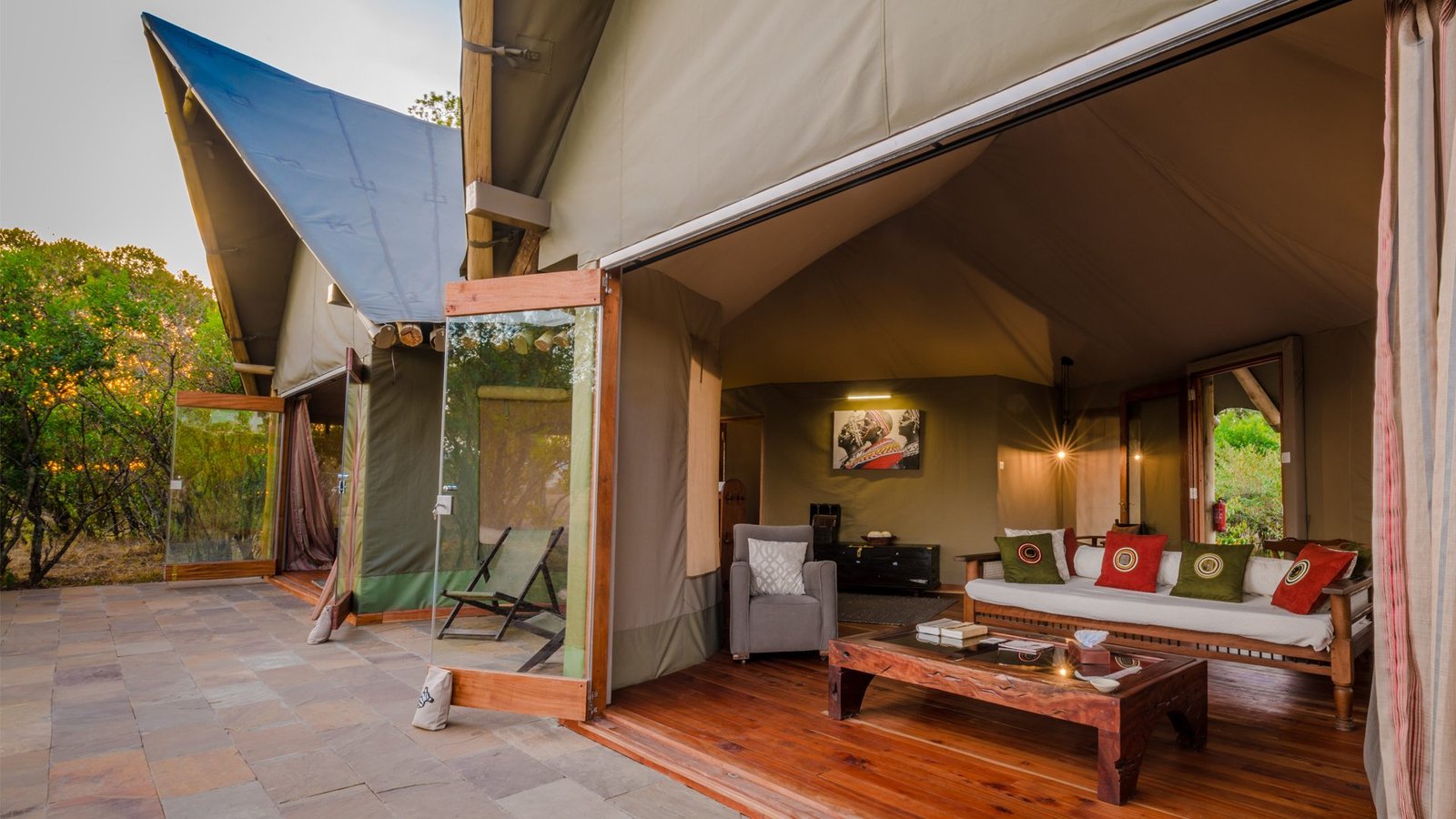 Luxury tented camp exterior at dusk with open glass panels and stone terrace