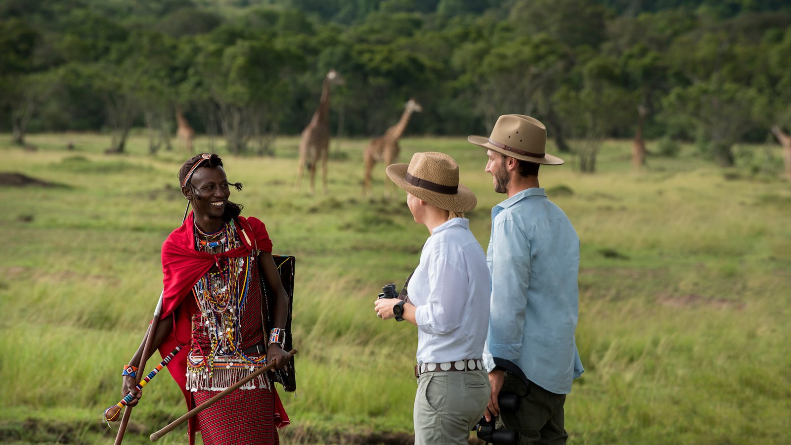 Guests on a walking safari with a Maasai guide, giraffe in the background